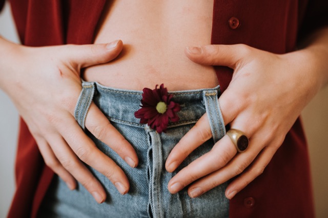 Une jeune femme place ses deux mains sur son ventre, pour faire un massage afin de soulager ses règles douloureuses naturellement. 