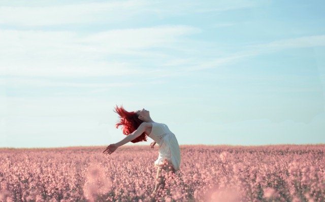 Une femme qui se sent libre, dans un champs, les bras vers le ciel. Elle parle librement de ses règles, sans tabou